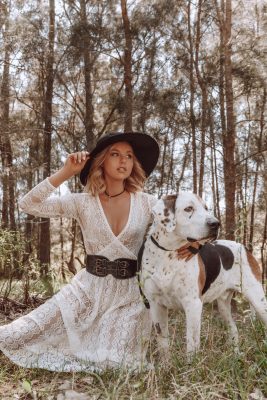 Woman in white dress holding a dog and her hat